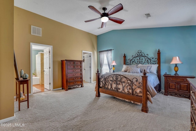 bedroom with vaulted ceiling, connected bathroom, light colored carpet, and ceiling fan