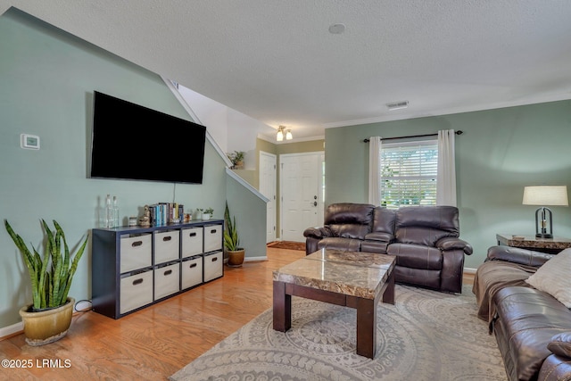 living room with crown molding, a textured ceiling, and light wood-type flooring