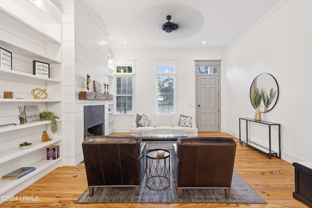 living room with a tile fireplace, ornamental molding, and light hardwood / wood-style flooring