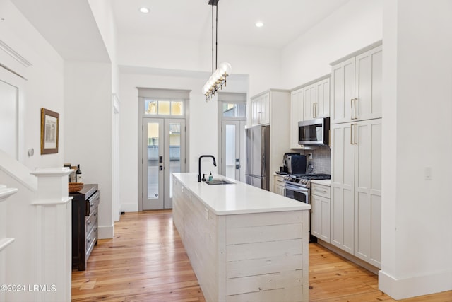 kitchen with sink, appliances with stainless steel finishes, decorative backsplash, a center island with sink, and decorative light fixtures