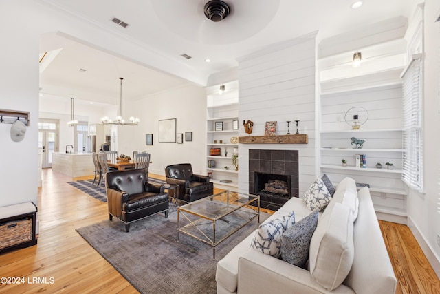 living room featuring a tiled fireplace, built in features, a chandelier, and light wood-type flooring