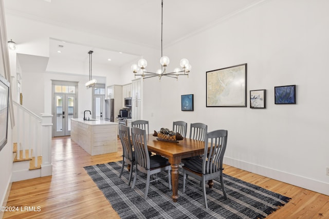 dining area with sink, crown molding, light hardwood / wood-style flooring, a notable chandelier, and french doors