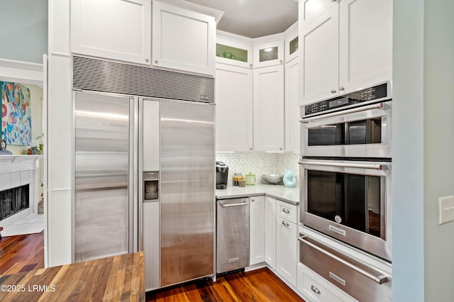 kitchen with dark wood-style flooring, a warming drawer, stainless steel appliances, tasteful backsplash, and white cabinets