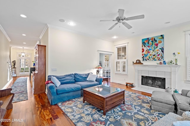 living room featuring ceiling fan, recessed lighting, wood finished floors, ornamental molding, and a tiled fireplace