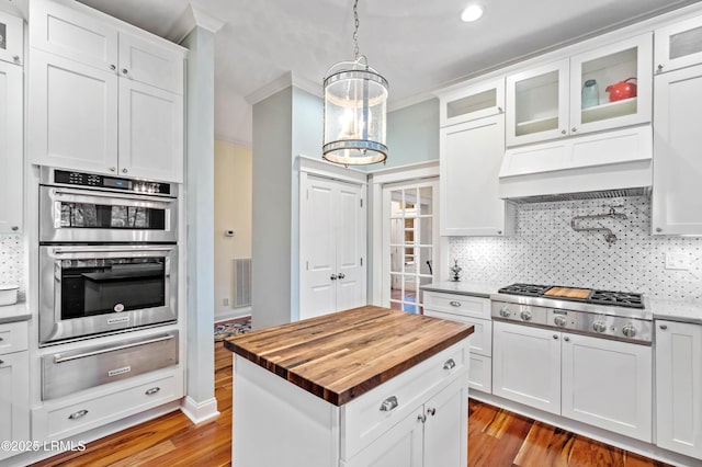 kitchen with a warming drawer, backsplash, appliances with stainless steel finishes, ventilation hood, and butcher block countertops