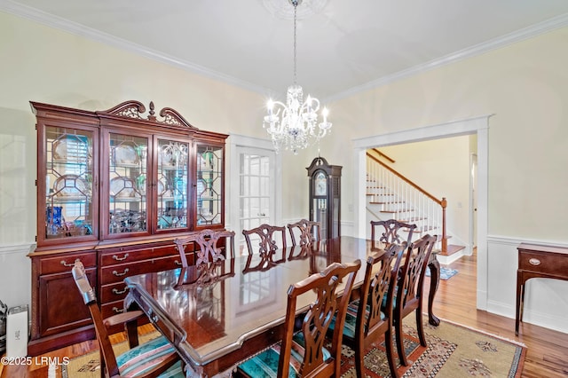 dining room featuring stairs, an inviting chandelier, light wood-style flooring, and crown molding