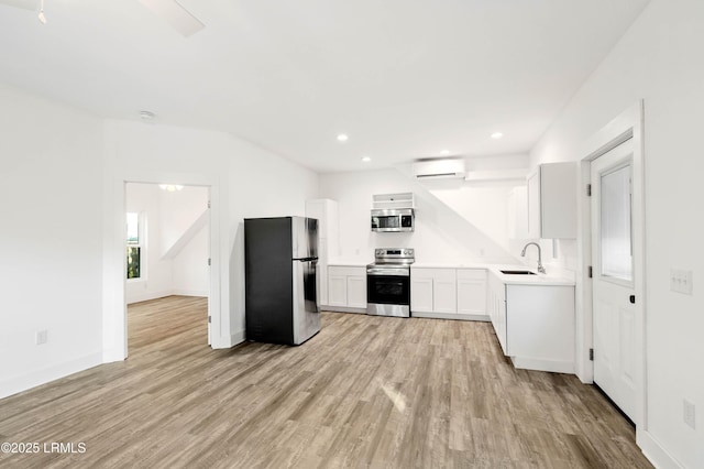 kitchen featuring light wood-type flooring, appliances with stainless steel finishes, a wall unit AC, and a sink