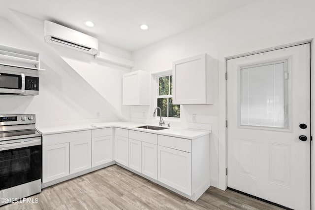 kitchen featuring stainless steel appliances, a sink, white cabinets, light wood-style floors, and a wall mounted AC