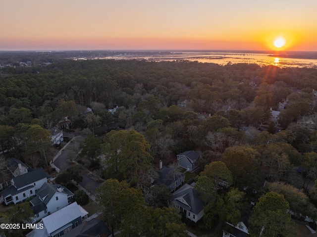 aerial view at dusk with a water view and a wooded view