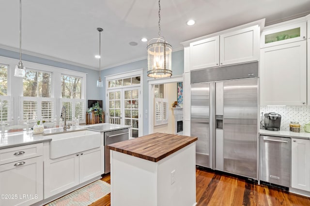 kitchen with dark wood finished floors, crown molding, appliances with stainless steel finishes, a sink, and butcher block countertops