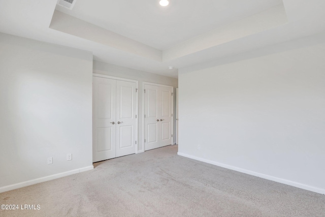 unfurnished bedroom with a tray ceiling, light colored carpet, and multiple closets