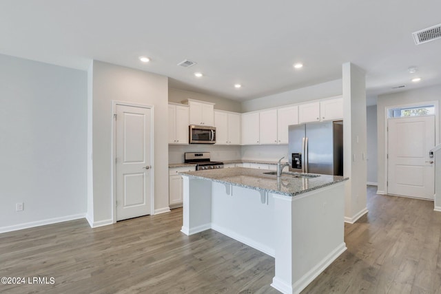 kitchen with sink, appliances with stainless steel finishes, white cabinetry, light stone counters, and a center island with sink