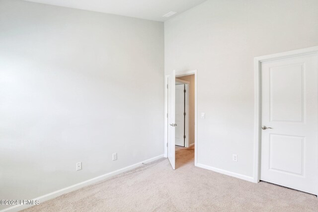 unfurnished bedroom featuring light carpet and a high ceiling