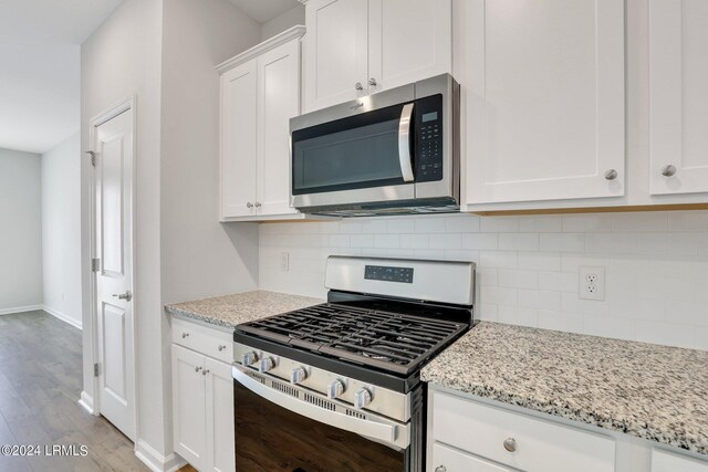 kitchen with appliances with stainless steel finishes, white cabinets, decorative backsplash, light stone countertops, and light hardwood / wood-style flooring