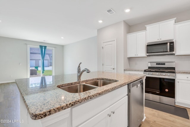 kitchen with sink, appliances with stainless steel finishes, white cabinetry, light stone counters, and a center island with sink