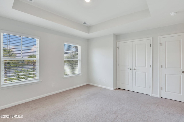 unfurnished bedroom with light colored carpet and a tray ceiling