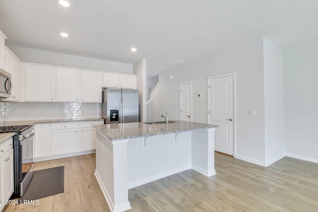 kitchen featuring appliances with stainless steel finishes, light stone countertops, a center island with sink, and white cabinets