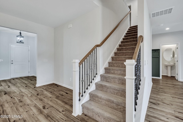 stairs featuring hardwood / wood-style flooring, sink, and a notable chandelier