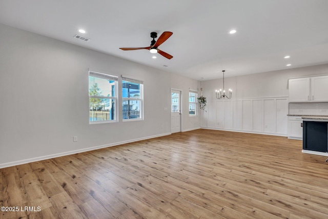 unfurnished living room featuring ceiling fan with notable chandelier and light wood-type flooring