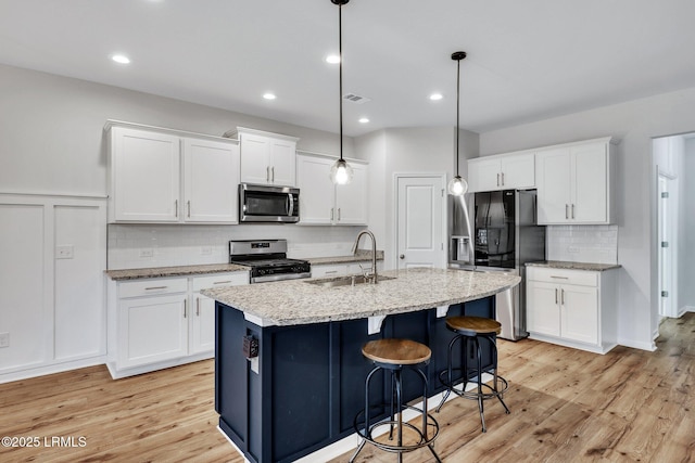 kitchen featuring sink, white cabinets, hanging light fixtures, stainless steel appliances, and a center island with sink