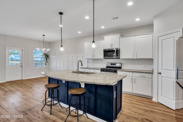 kitchen featuring stainless steel appliances, white cabinetry, sink, and a center island with sink