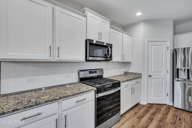 kitchen featuring tasteful backsplash, white cabinetry, dark stone countertops, stainless steel appliances, and light wood-type flooring