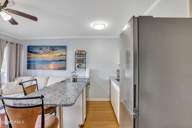 kitchen with stainless steel appliances, white cabinets, ornamental molding, and light wood-style flooring