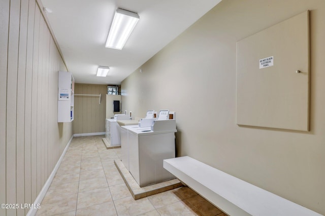 community laundry room with wood walls, independent washer and dryer, and light tile patterned flooring