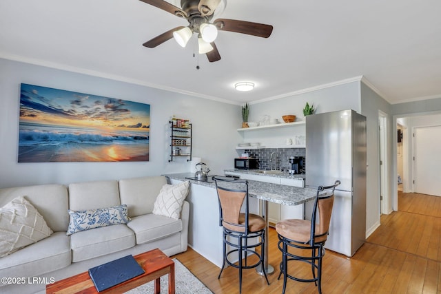 living area with light wood-type flooring, a ceiling fan, and crown molding