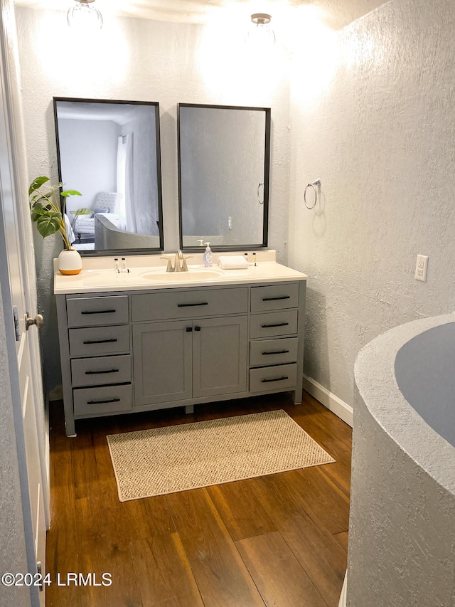 full bathroom featuring wood finished floors, baseboards, a textured wall, and double vanity