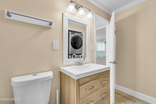 bathroom featuring crown molding, stacked washer / dryer, vanity, wood-type flooring, and toilet