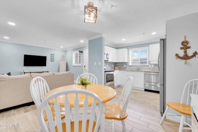 dining space with ornamental molding, sink, and light wood-type flooring