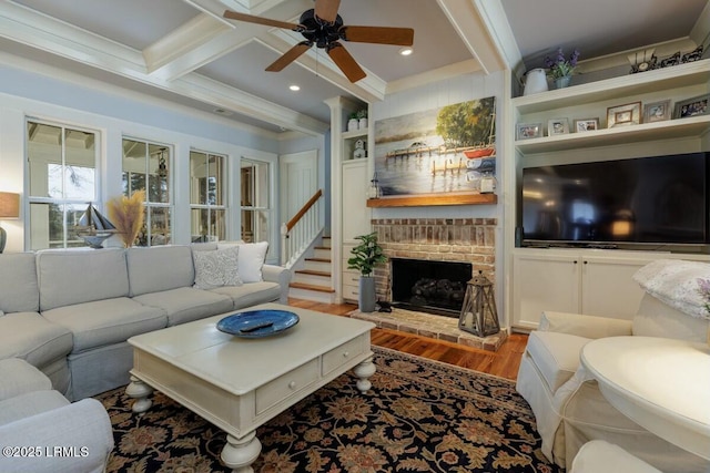 living area with built in features, ceiling fan, wood finished floors, a fireplace, and beam ceiling