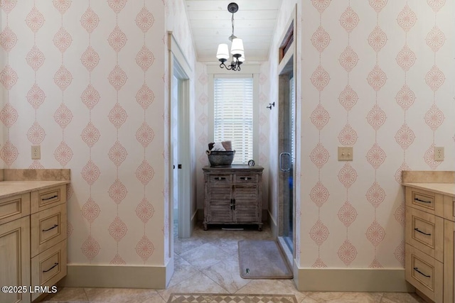 bathroom with a notable chandelier, a stall shower, vanity, baseboards, and tile patterned floors