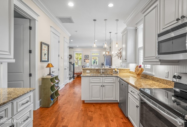 kitchen with visible vents, a peninsula, a sink, appliances with stainless steel finishes, and crown molding