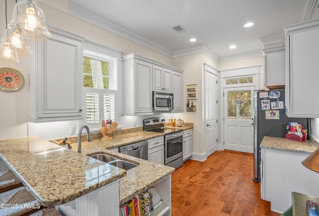 kitchen featuring a breakfast bar area, a peninsula, a sink, appliances with stainless steel finishes, and crown molding