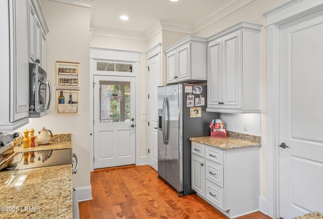 kitchen featuring ornamental molding, light stone counters, recessed lighting, appliances with stainless steel finishes, and wood finished floors