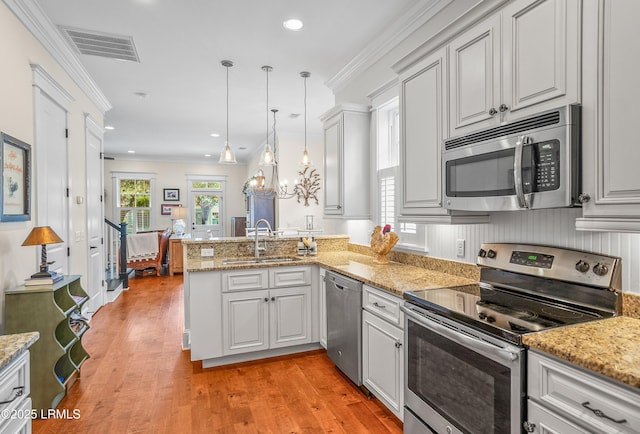 kitchen featuring ornamental molding, a sink, appliances with stainless steel finishes, a peninsula, and light wood finished floors