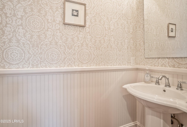 bathroom featuring wallpapered walls, a wainscoted wall, and a sink