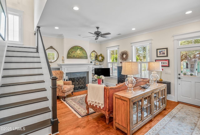 living area with stairway, a fireplace with flush hearth, ornamental molding, recessed lighting, and light wood-style floors