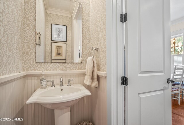 bathroom with a wainscoted wall, wallpapered walls, wood finished floors, and ornamental molding