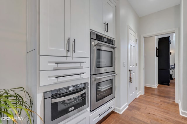 kitchen featuring white cabinetry, light hardwood / wood-style floors, and stainless steel double oven