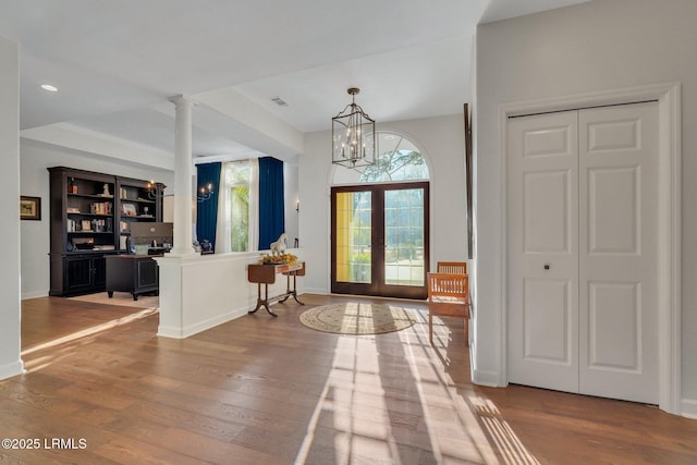 entryway featuring decorative columns, wood-type flooring, an inviting chandelier, and french doors