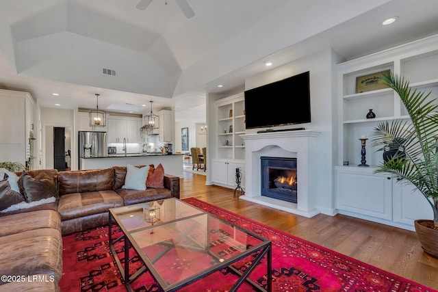 living room with built in shelves, ceiling fan, lofted ceiling, and hardwood / wood-style flooring