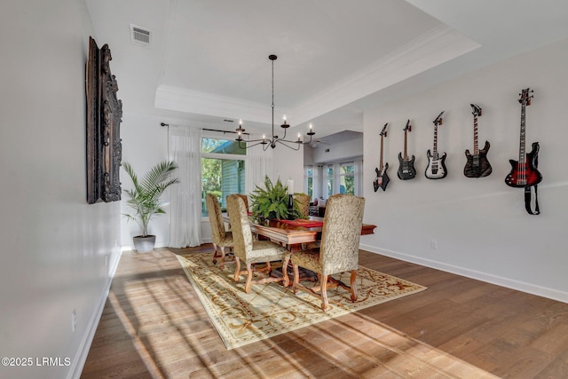 dining space with a raised ceiling, wood-type flooring, and an inviting chandelier