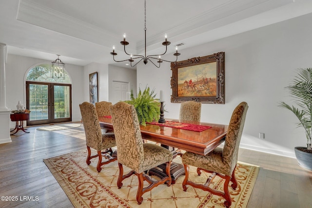 dining space featuring a chandelier, hardwood / wood-style flooring, ornamental molding, a raised ceiling, and french doors