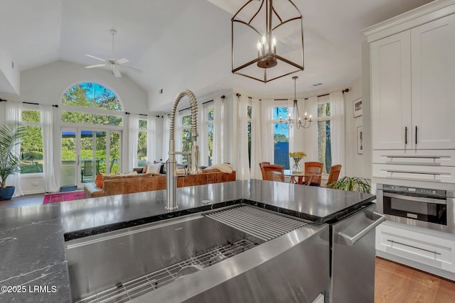 kitchen with lofted ceiling, sink, dark stone counters, oven, and white cabinets