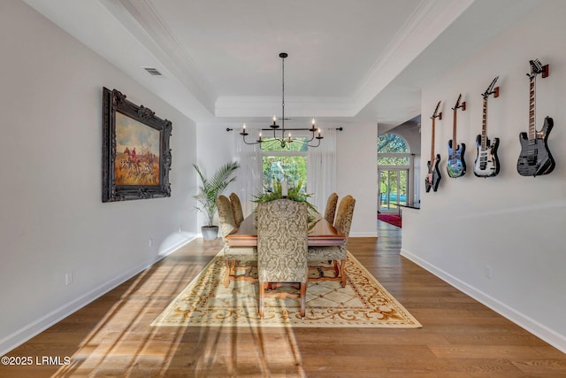 dining area featuring an inviting chandelier, ornamental molding, wood-type flooring, and a tray ceiling