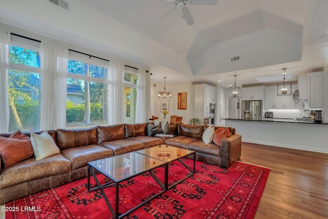 living room with a tray ceiling, vaulted ceiling, light hardwood / wood-style floors, and ceiling fan with notable chandelier