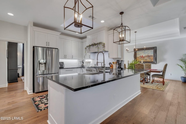 kitchen with decorative light fixtures, white cabinets, stainless steel fridge, decorative backsplash, and light hardwood / wood-style floors